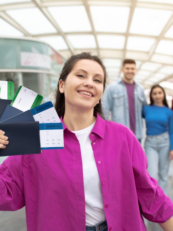 Flight Offer. Cheerful Lady Tourist Showing Boarding Passes Tickets Posing With Friends Standing At Airport, Smiling At Camera And Advertising Cheap Transportation Offer. Selective Focus